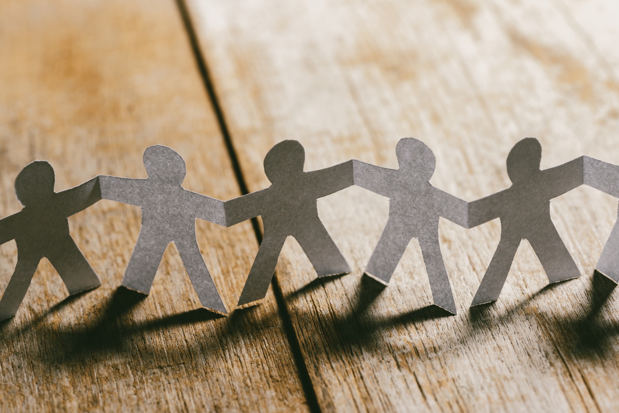 Paper People Holding Hands on a wooden table.